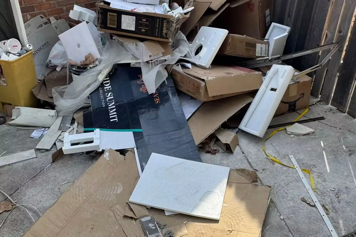 Broken cabinets, sinks and cardboard piled against a brick wall