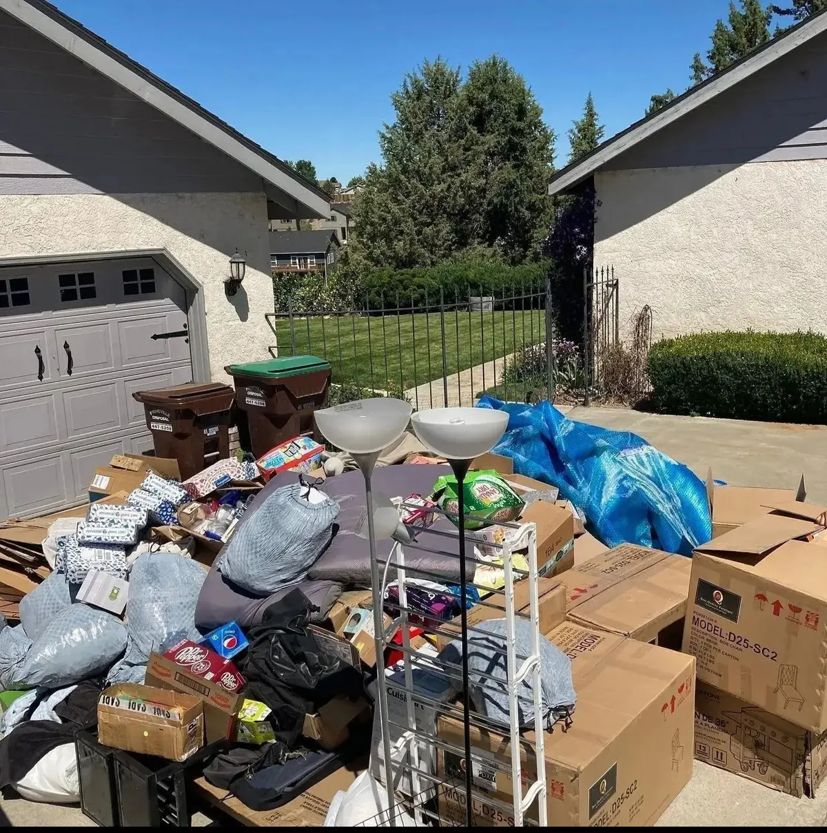 Boxes, bags and lamps stacked in a driveway outside a garage