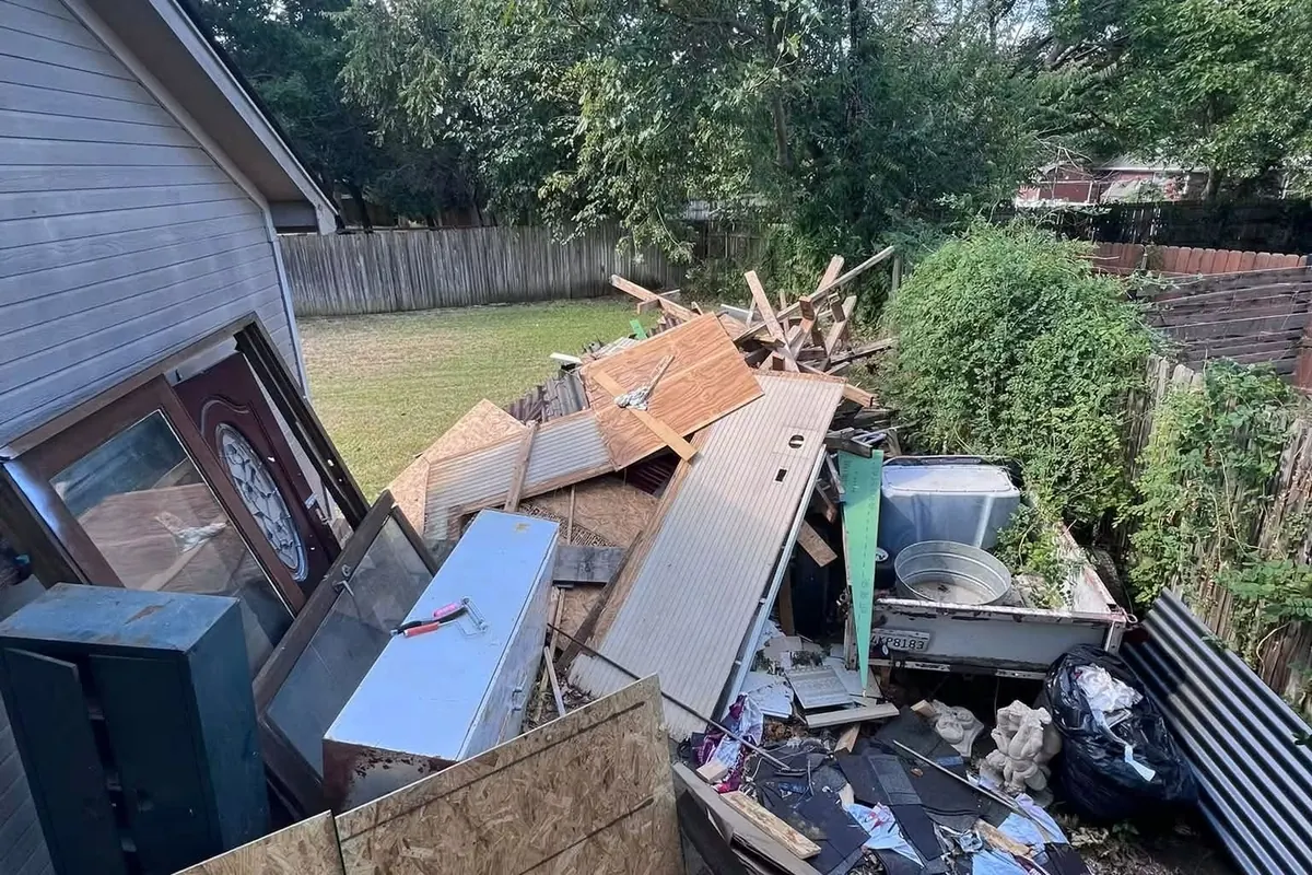 Old panels, a file cabinet and yard debris piled beside a house